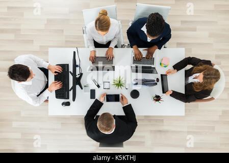 High Angle View Of Businesspeople Working On Computers And Laptops In Office Stock Photo