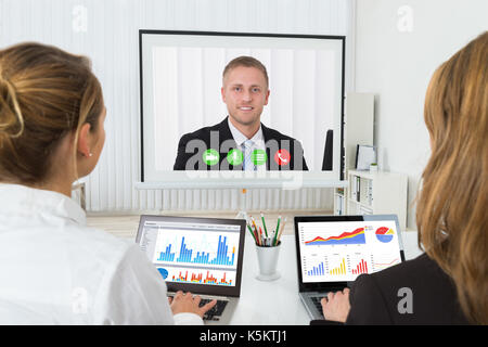 Two Businesswomen With Graphs On Laptop Videoconferencing In Office Stock Photo