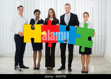 Group Of Businesspeople Holding Multi-colored Puzzle Pieces In Office Stock Photo
