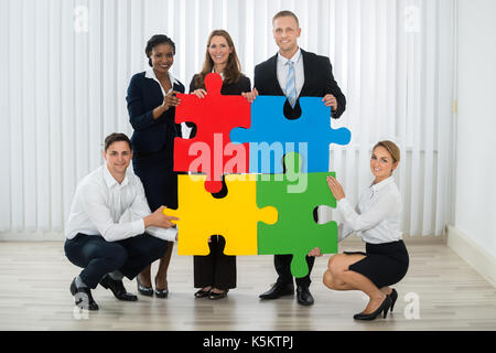 Group Of Businesspeople Holding Multi-colored Puzzle Pieces In Office Stock Photo