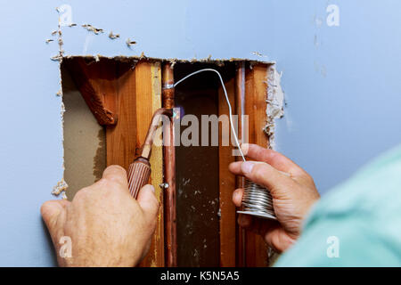 metal pipes and fittings of domestic water supply system seen through a hole in a white wall plumber repairs the pipe in the wall Stock Photo