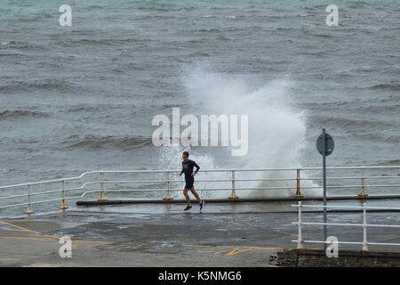 Aberystwyth Wales UK, Sunday  10 September 2017  UK Weather: Strong wind and stormy seas batter the seaside in Aberystwyth on the coast of Cardigan Bay in west Wales.   pictured: A jogger narrowly avoids a soaking as he runs along the promenade  A Met Office ‘yellow’ warning has been issued for south western regions of the UK, with widespread gale force winds and gusts of up to 60mph expected during Monday morning. Credit: keith morris/Alamy Live News Stock Photo