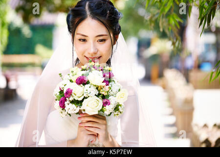 beautiful and happy young asian bride wearing bridal veil holding a bunch of flower Stock Photo