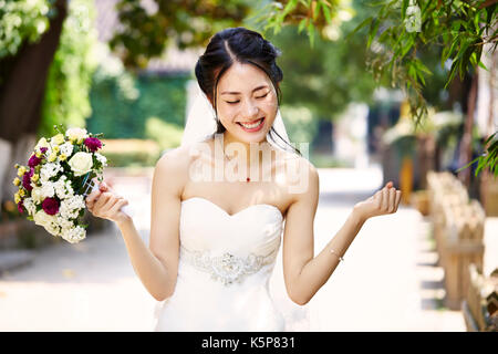 young and beautiful asian bride rejoicing with bouquet in hand. Stock Photo