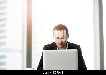Smart businessman looking at laptop screen with thoughtful facia Stock Photo