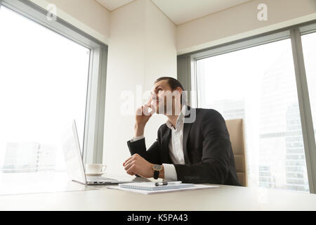 Dreamy young handsome businessman in deep thought about corporat Stock Photo