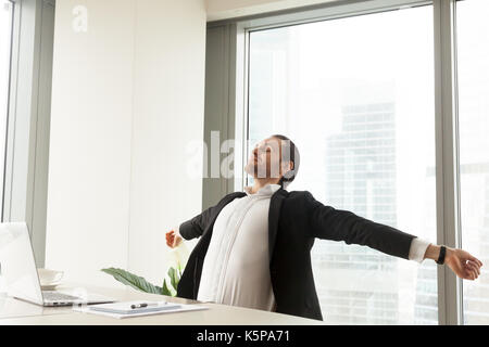 Smiling businessman stretching at workplace in modern office. Stock Photo