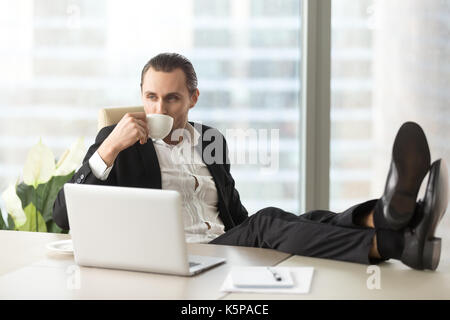 Businessman relaxing and drinking coffee at workplace in office. Stock Photo