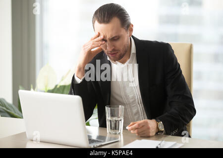 Sick businessman having severe headache, holding painkiller reme Stock Photo