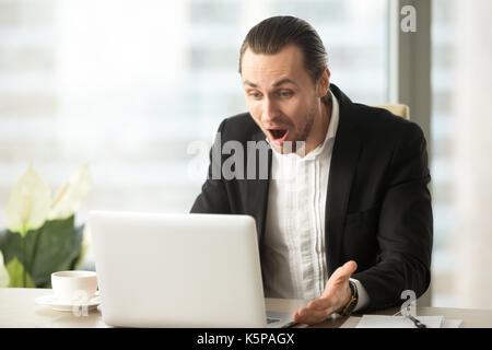 Frustrated young businessman looks at laptop screen screaming in Stock Photo