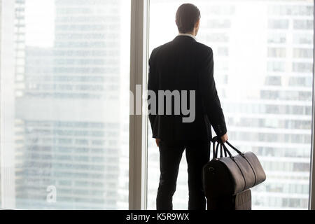 Businessman with luggage standing in front of large window. Stock Photo