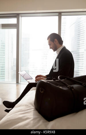 Young smiling businessman working on laptop in bedroom. Stock Photo