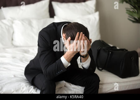 Stressed upset businessman sitting on bed, having headache. Stock Photo