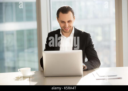 Smiling handsome businessman working on laptop in office. Stock Photo