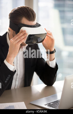 Businessman wears vr glasses looking at laptop screen. Stock Photo