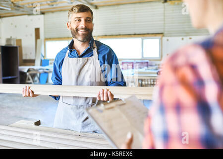 Cheerful middle-aged craftsman and his unrecognizable colleague making inventory at spacious warehouse Stock Photo
