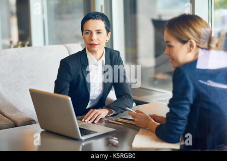 Team of talented managers brainstorming on start-up project while having working meeting at cozy small coffeehouse, view through panoramic window Stock Photo