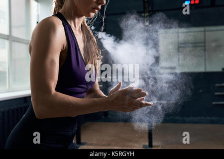 Side view closeup of young  woman covering hands with talk in dark gym preparing for heavy weightlifting Stock Photo
