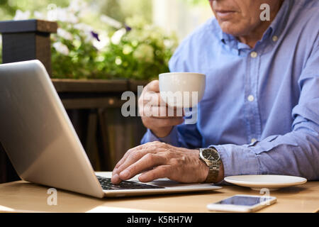 Closeup image of unrecognizable senior man using laptop computer in cafe outdoors holding coffee cup Stock Photo