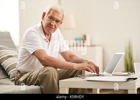 Portrait of modern senior man using laptop at home and smiling Stock Photo