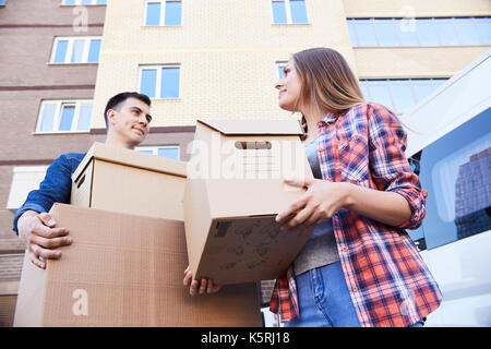 Low angle portrait of happy couple holding cardboard boxes while moving into new home, outdoors Stock Photo