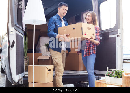 Portrait of smiling young man and woman unloading boxes and furniture from moving van outdoors Stock Photo