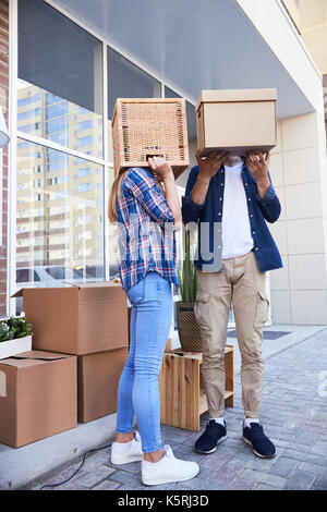 Portrait of unrecognizable young couple with boxes on heads having fun while unloading moving van outdoors Stock Photo