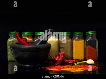 A set of jars with spices and mortar with red pepper on a black background Stock Photo