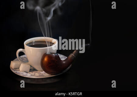 A beautiful black coffee in a white cup with sugar and a smoking pipe on a black background. A wonderful set for a good evening rest Stock Photo