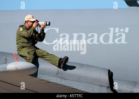 Crew member of a Royal Canadian Air Force CP-140 Aurora sitting on the wing of his aircraft with a camera and taking photographs at an airshow Stock Photo