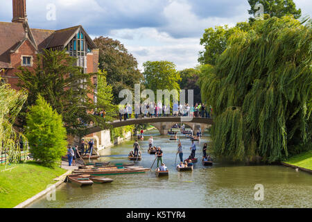 Tourists crossing a bridge over River Cam with punters underneath and the Jerwood Library on the left, Cambridge, UK Stock Photo