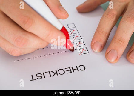 Close-up Of Person Hand Marking On Checklist Form With Red Marker Stock Photo