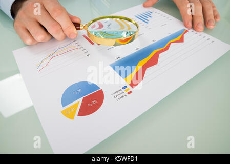 Businessman Analyzing Graph Through Magnifying Glass In Office Stock Photo