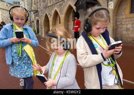 Three sisters /children /kid /kids on holiday listen to an audio guide information while on a tour inside the walls of Windsor Castle, Berkshire UK.