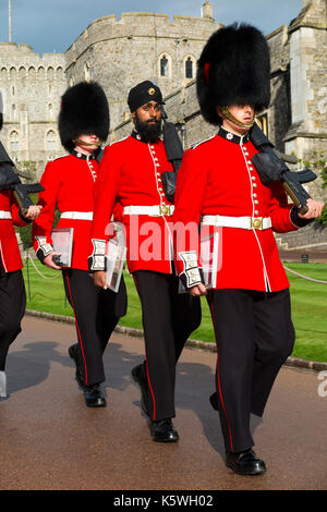 British Army soldiers / Windsor Castle Guard ( Coldstream Guards ) wearing traditional red uniform & Bearskin hat / Bearskins & Sikh turban on Gdmn Lall. Stock Photo