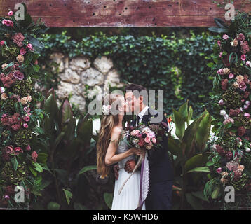 Amazing wedding ceremony with a lot of fresh flowers in Rustic style. Happy newlyweds kissing Stock Photo