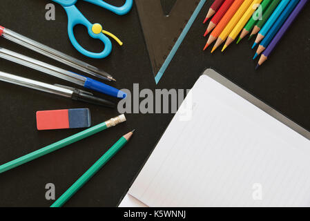 Different Kinds of School and Office Utensils on a Dark Chalkboard Surface with a Blank Notebook Stock Photo