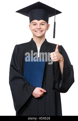 Graduate teen boy student in black graduation gown with hat, holding diploma and showing thumb up gesture - isolated on white background. Child back t Stock Photo