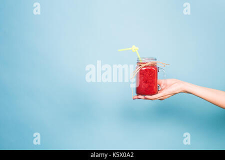 Woman's hand holding glass of strawberry and rasberry smoothie on blue background Stock Photo