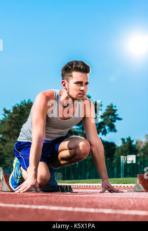 Track and field sprinter on starting point at cinder track in sports arena Stock Photo