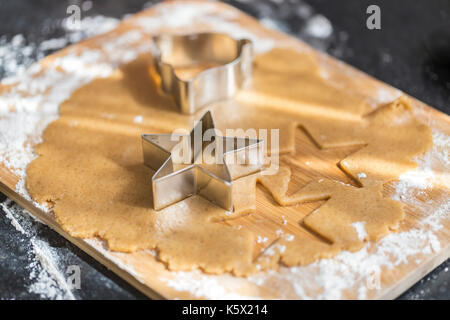 Making gingerbread cookies. Gingerbread dough with star shapes and a cutter on a wooden board. Stock Photo