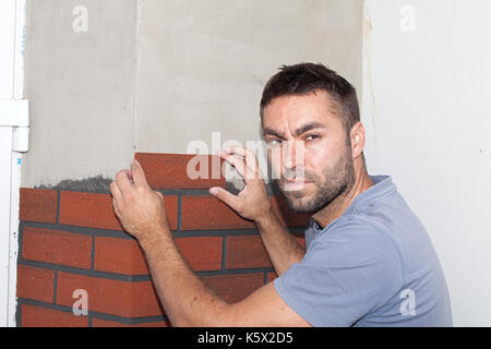 Reconstruction of the house. Worker stuck brick cladding (imitation brick) on the outside facade. Finishing work on the new facade. Stock Photo