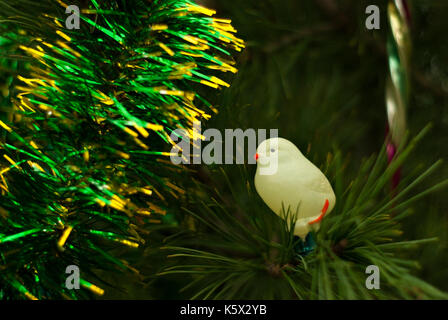 Vintage glass Christmas tree toy: cute light yellow chicken closeup against the background of green branches. Blurred background. Stock Photo