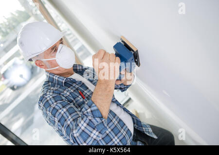 aged builder in hardhat sanding wall indoors Stock Photo