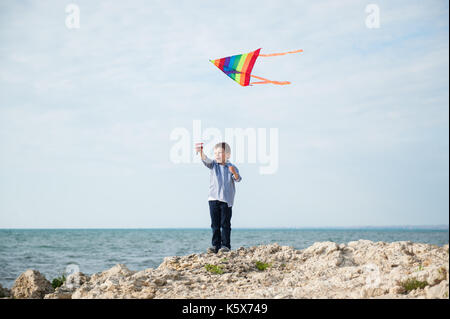 happy small boy holding a kite flying in the sky on the background of sea Stock Photo