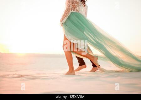 Legs of bride and groom walking barefoot on sand in desert at sunset. Close up. Stock Photo