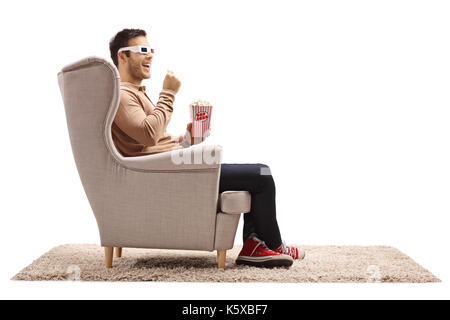 Young man seated in an armchair wearing a pair of 3D glasses and having popcorn isolated on white background Stock Photo