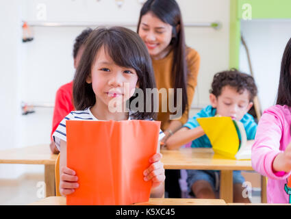 Asian girl kid reading book in classroom and while teacher teach friends beside them,kindergarten education preschool. Stock Photo