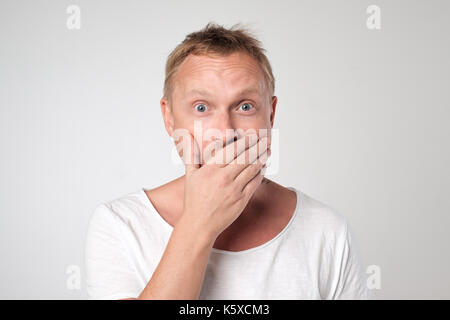 young caucasian man shows sign hand gesture holding finger on lips. Stock Photo
