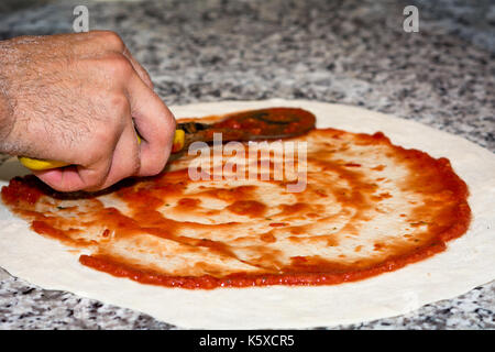 Prepared pizza dough with tomato sauce. selective focus.close-up of man hands in action Stock Photo